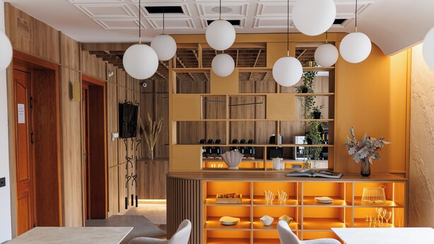 A modern interior with a wooden reception desk, white pendant lights, and a seating area with tables and chairs.