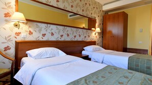 A hotel room with two beds, a wooden headboard, floral wallpaper, and two wall-mounted lamps.