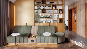 A modern reception area with a curved green sofa, a small round table, and a wooden shelving unit with various items.
