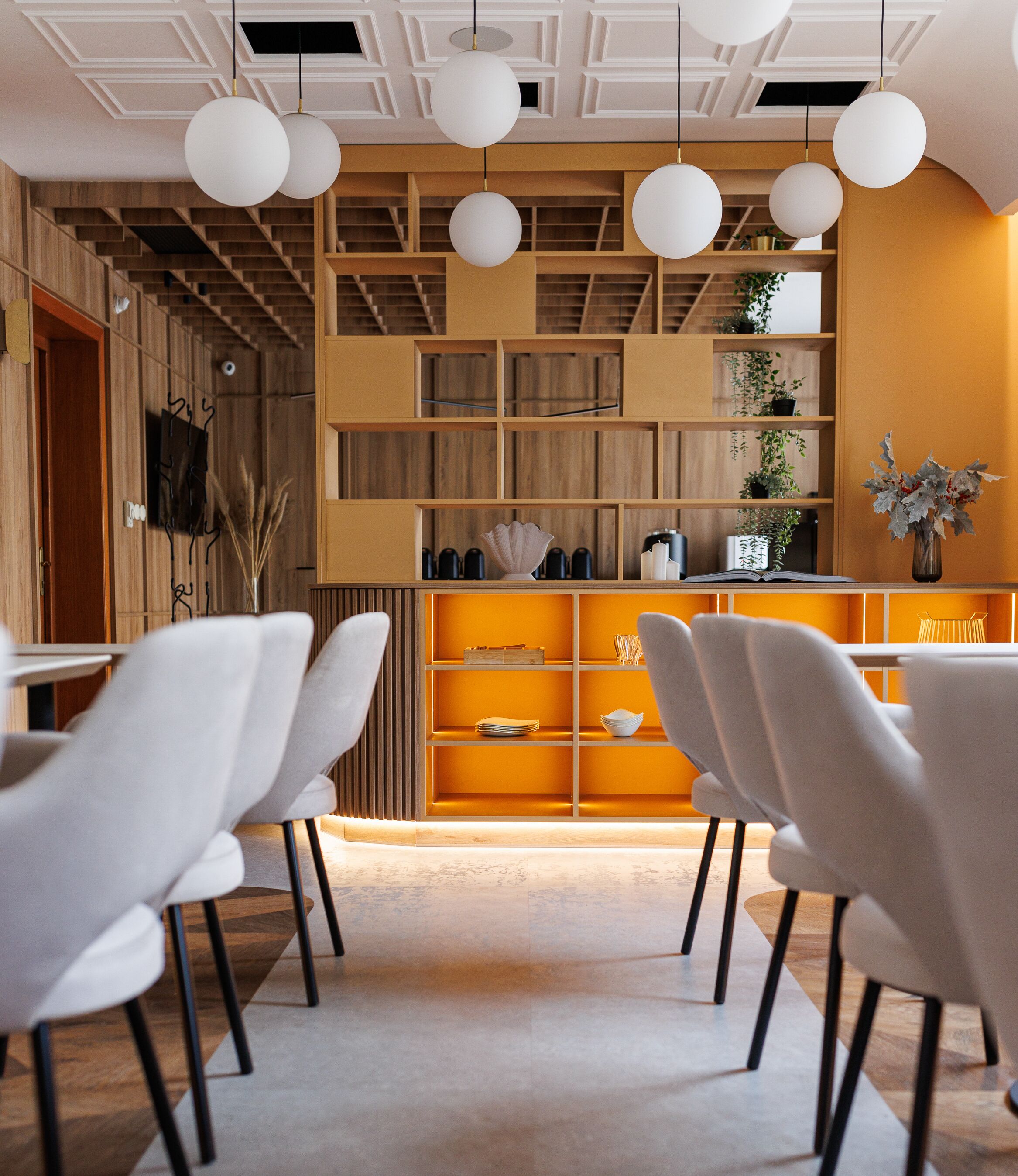 Een moderne eetruimte met witte stoelen, een houten boekenkast en hanglampen.