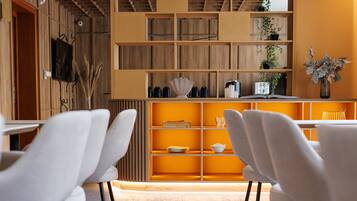 A modern dining area with white chairs, a wooden bookshelf, and pendant lighting.