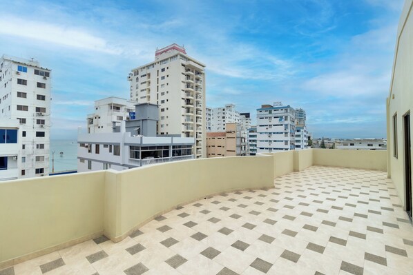 Una terraza en la azotea con suelo estampado, rodeada de edificios altos y un cielo despejado.
