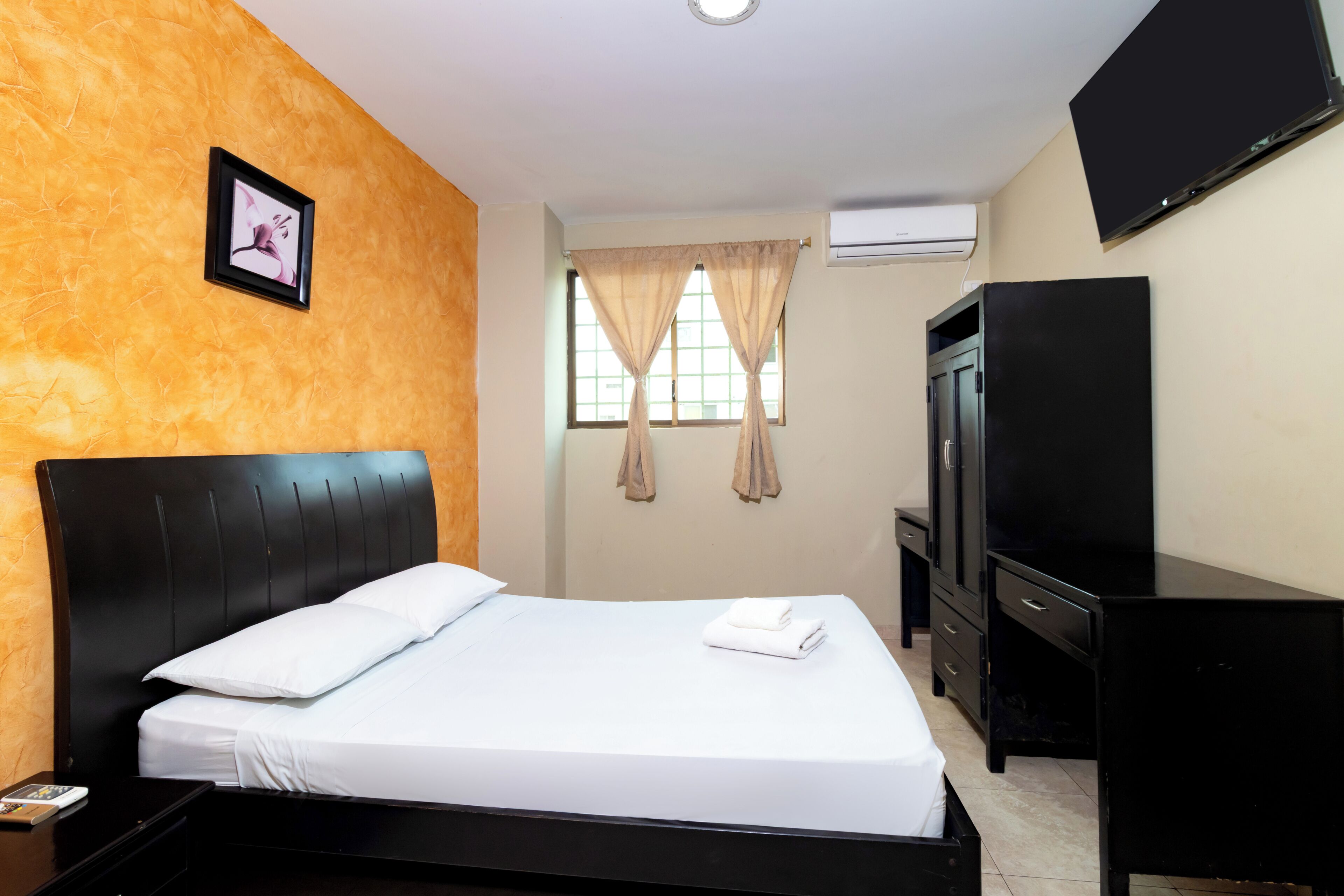 Quarto de hotel com cama, televisão, guarda-roupa e janela com cortinas.