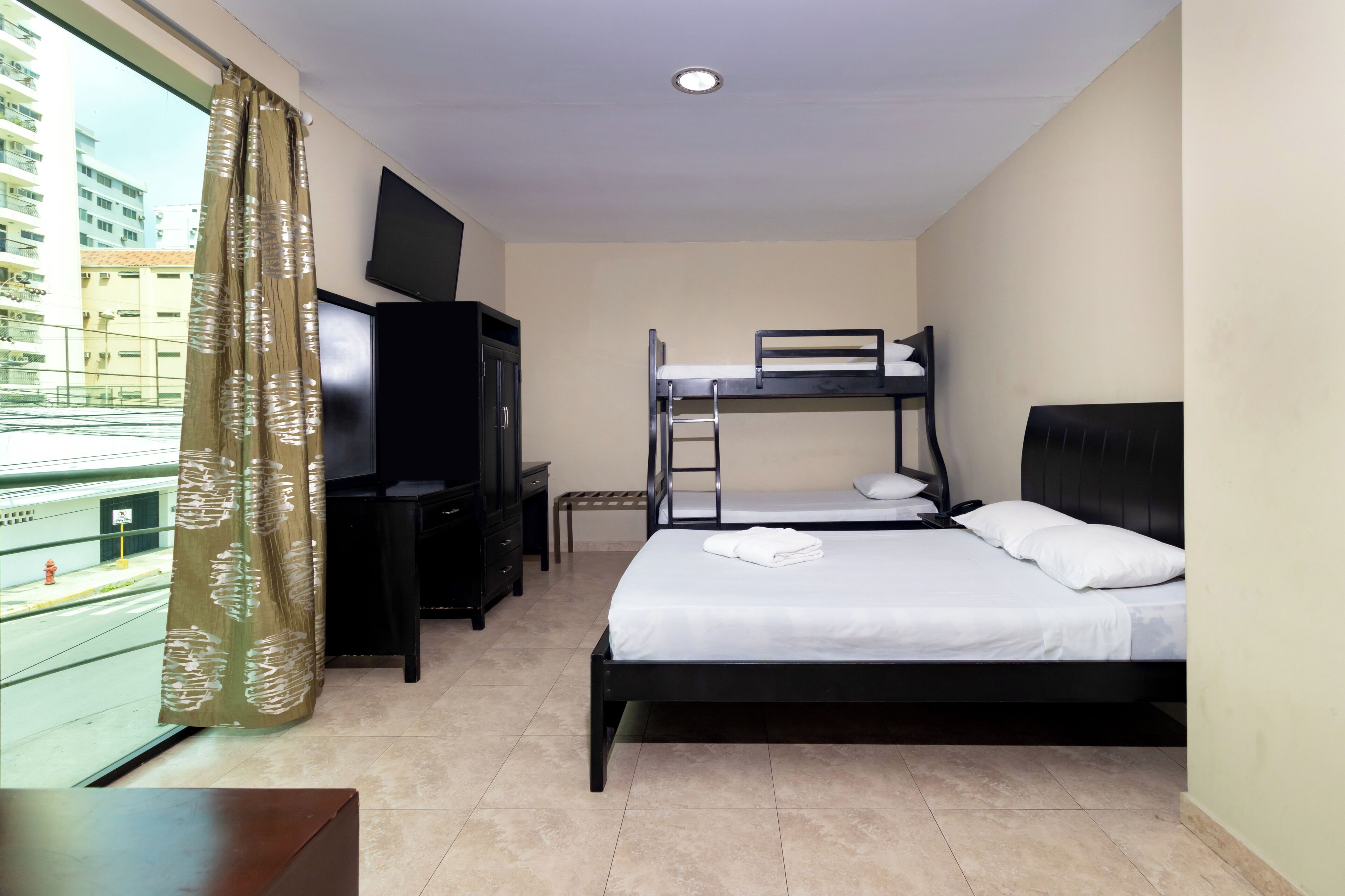 A hotel room with a bunk bed, a desk with a chair, a television, and a window with curtains.