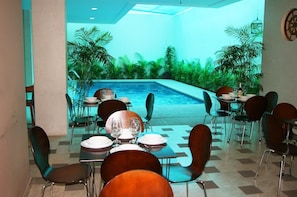 Un comedor con mesas y sillas, una piscina con vistas a la vegetación y un techo con tragaluces.