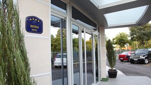 A hotel entrance with a sign reading "XOTEA HOTEL" and a parking area with several cars. - Garni Hotel Zeder (Belgrade)