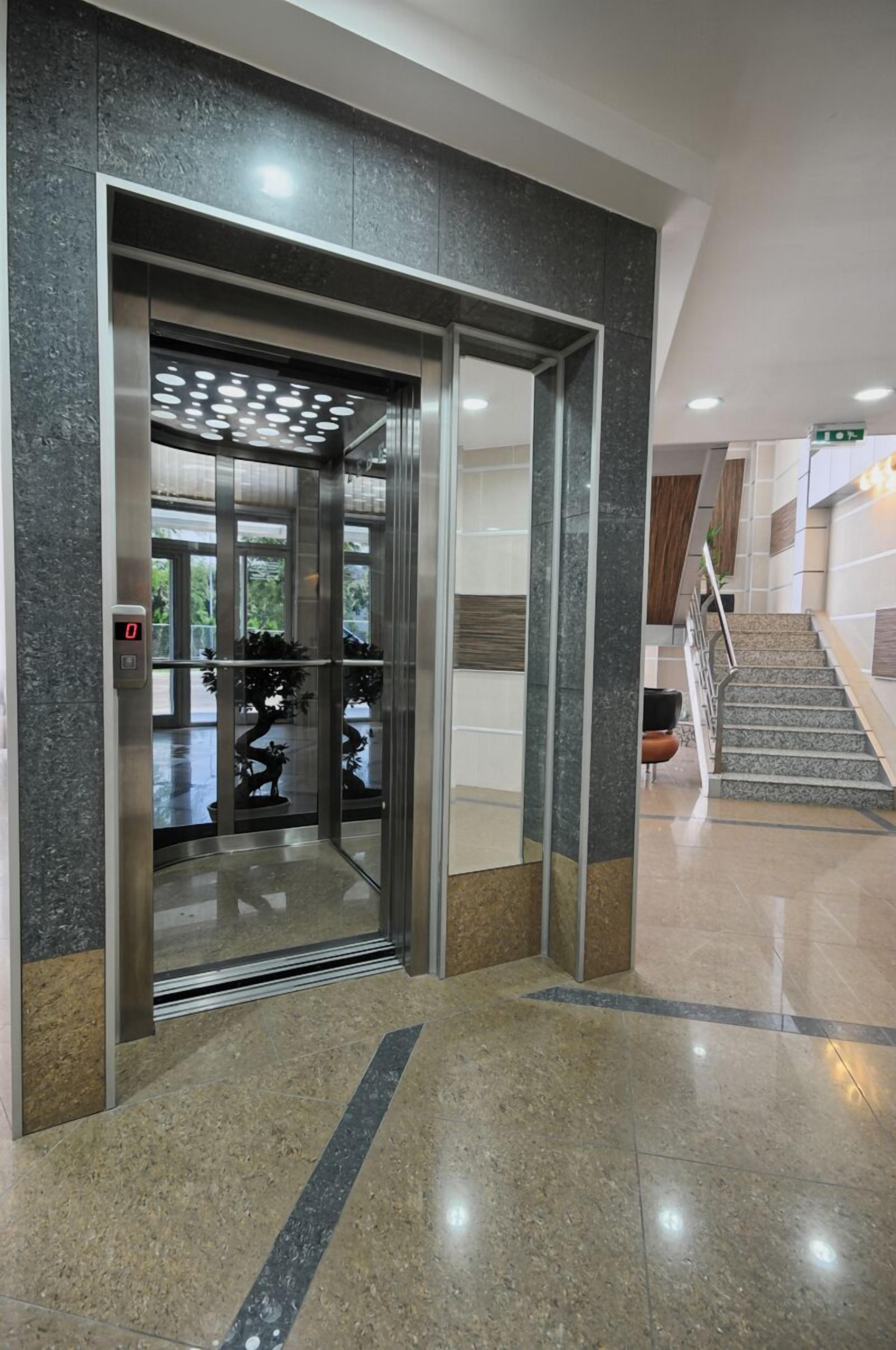 An elevator with a digital display, a staircase, and a polished marble floor.