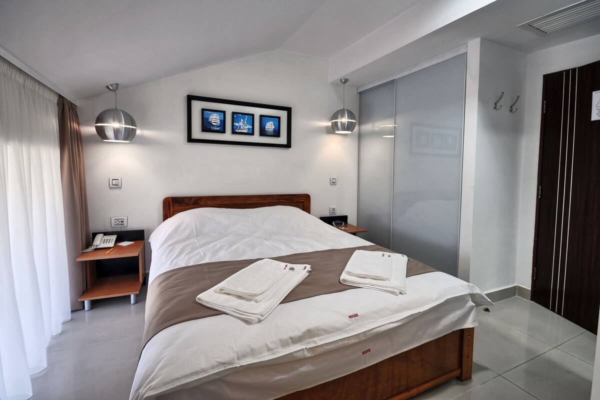 A modern hotel room with a wooden bed, two bedside tables, a nightstand, a wardrobe, and a framed picture on the wall.