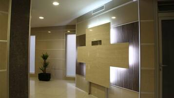 A hallway with a modern design, featuring a large cross-shaped wall decoration, a potted plant, and a door on the right.