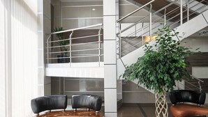 A modern lobby with a glass coffee table, leather chairs, a staircase, and a potted plant. - Garni Hotel Zeder (Belgrade)