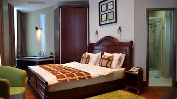 Habitación de hotel con una cama grande, un escritorio con silla, un sillón verde, un armario de madera y una zona de ducha.