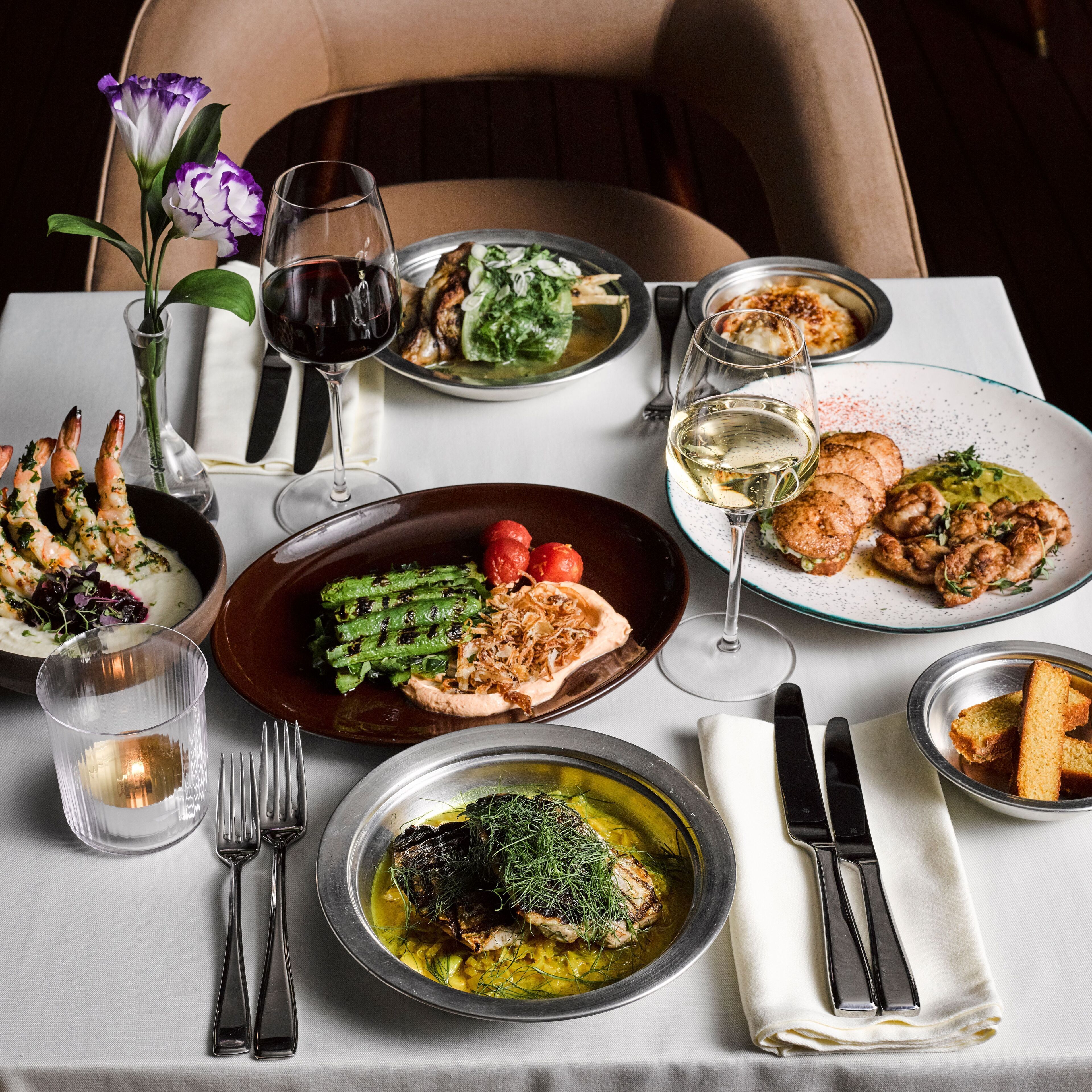 A dining table set with various dishes, wine glasses, and cutlery.