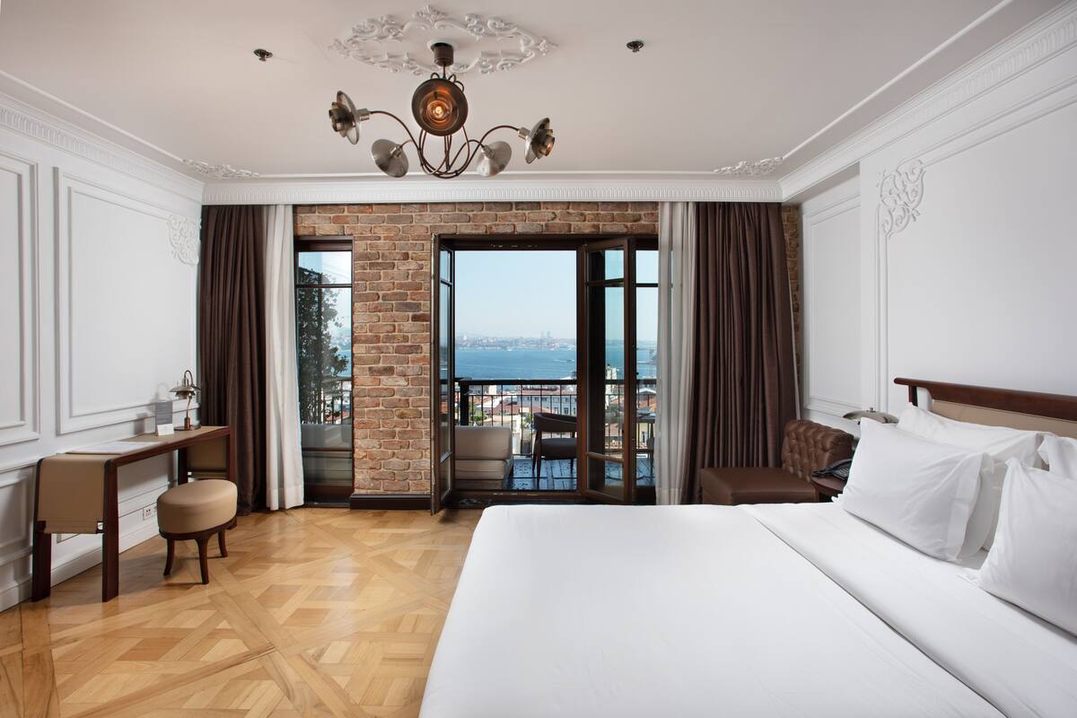 A hotel room with a large bed, a desk, and a view of the sea through a glass door.