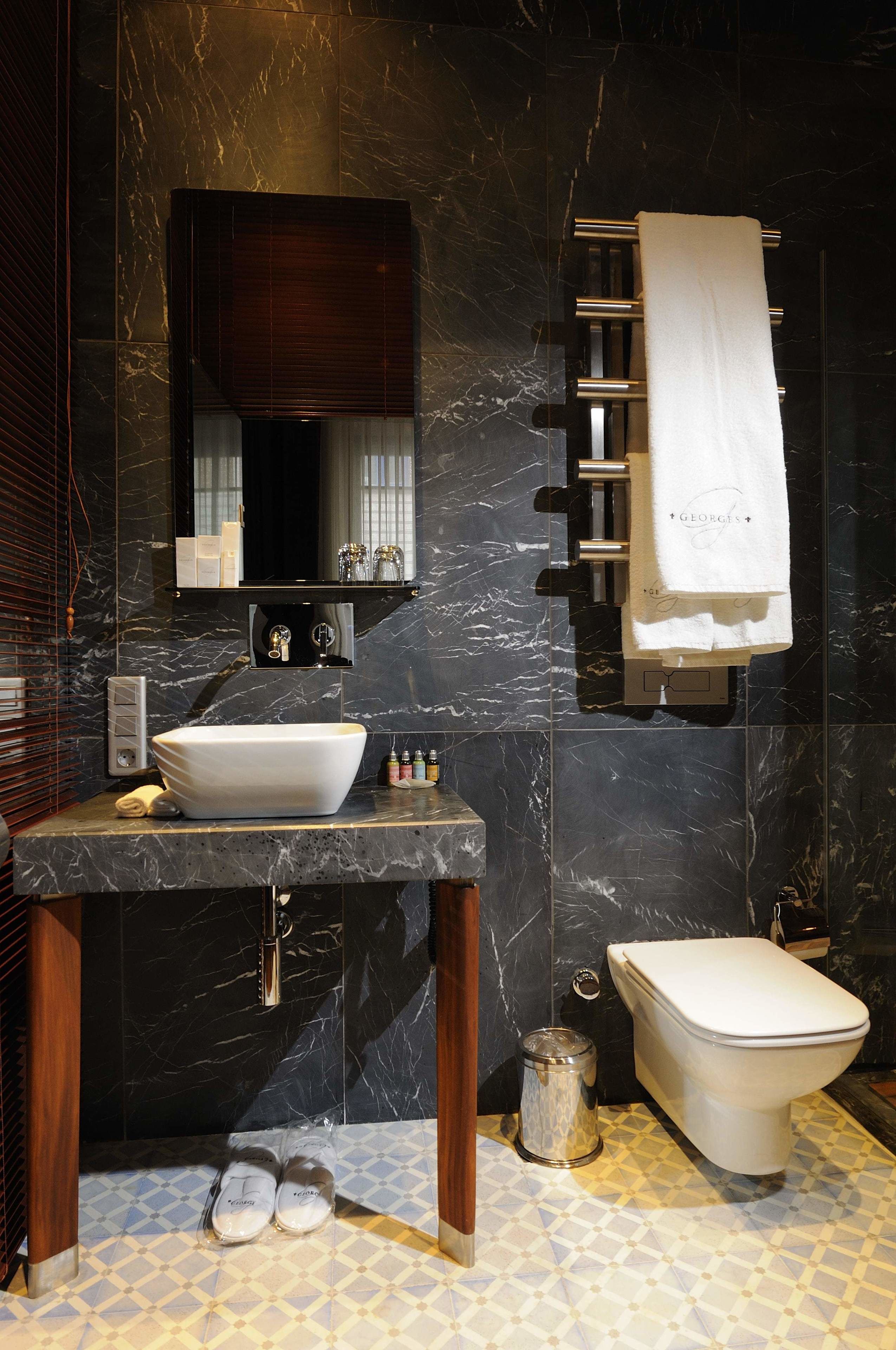 A modern bathroom with a marble sink, a large mirror, a towel rack, and a toilet.