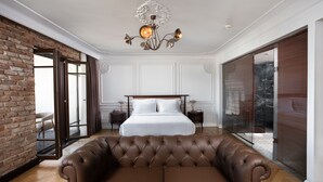 Une chambre spacieuse avec un grand lit, un canapé en cuir, un lustre et un mur en briques.