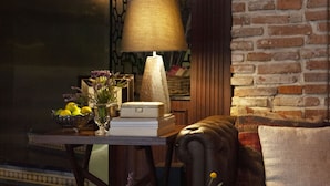 Un salon chaleureux avec un mur en briques, un canapé confortable, une table basse en bois avec une lampe, des livres et un vase rempli de fleurs.