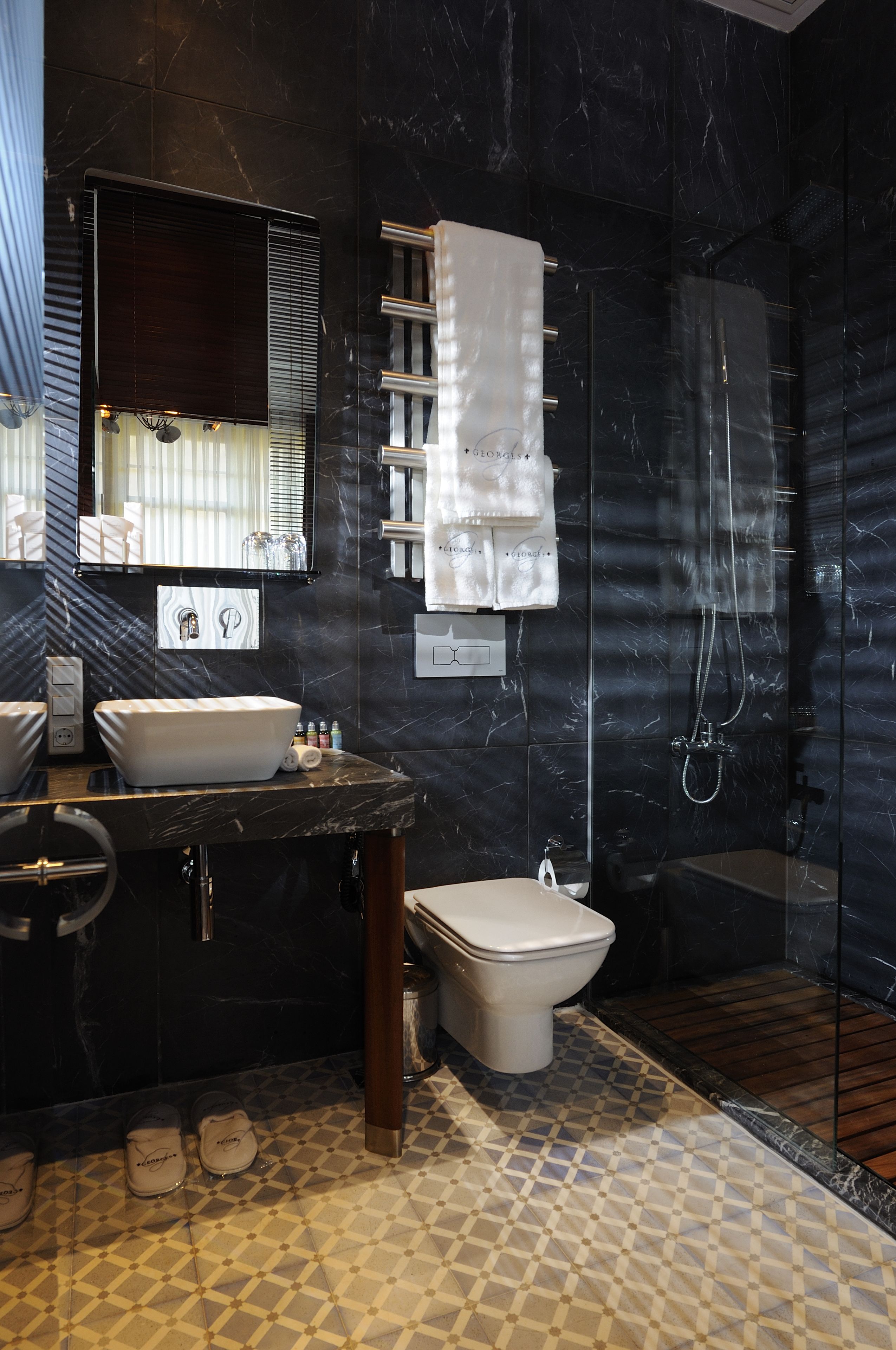 A modern bathroom with a dark marble wall, a white sink, a toilet, and a glass-enclosed shower.