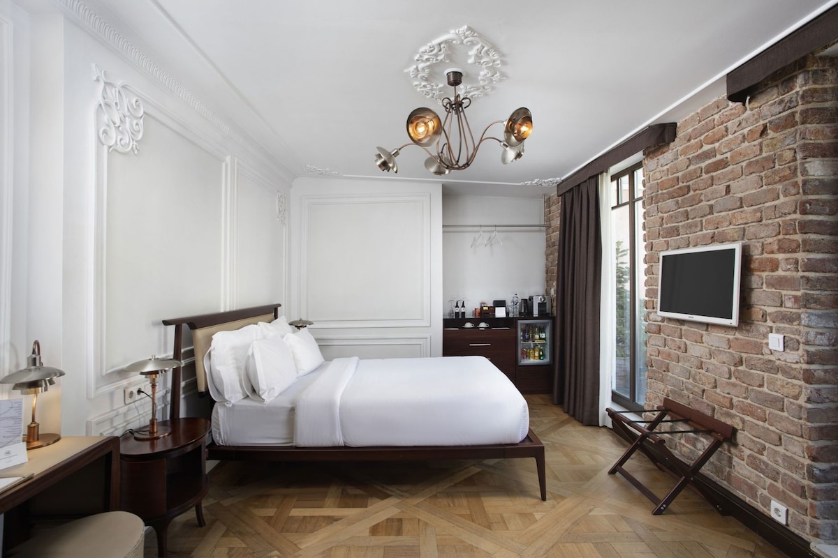 Habitación de hotel con cama, escritorio, silla, televisor, candelabro y pared de ladrillo.