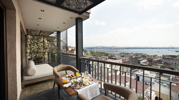 Un balcon avec une table à manger préparée pour le petit-déjeuner, un canapé et une vue sur la ville et l’eau.