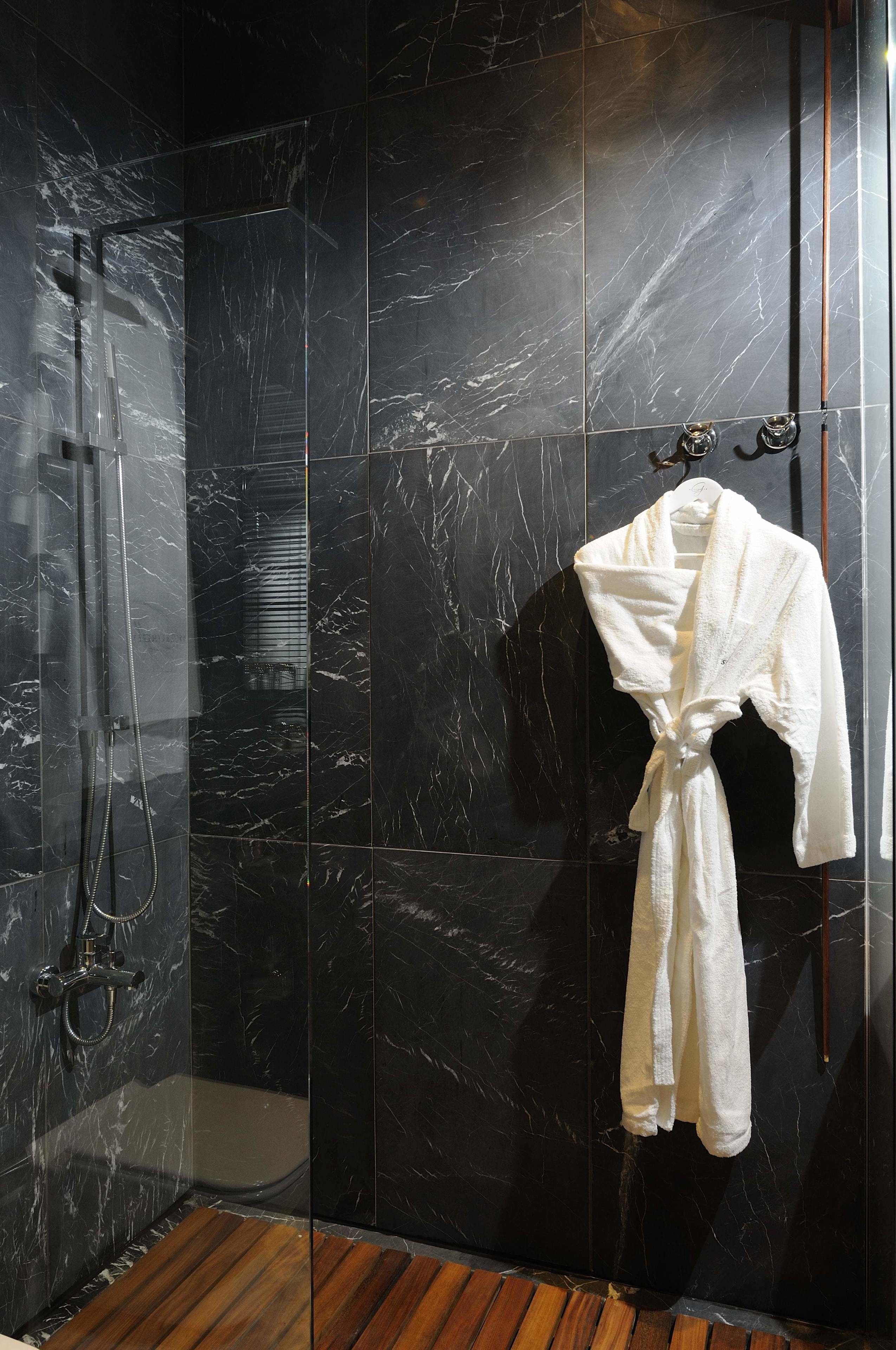 A modern bathroom with a glass-enclosed shower, marble walls, and a wooden floor.