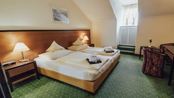 A hotel room with a large bed, two bedside tables with lamps, a small table with a vase, and a window with curtains.