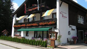 Hotel de dois andares com varandas decoradas com flores, área de estar externa e toldo verde.