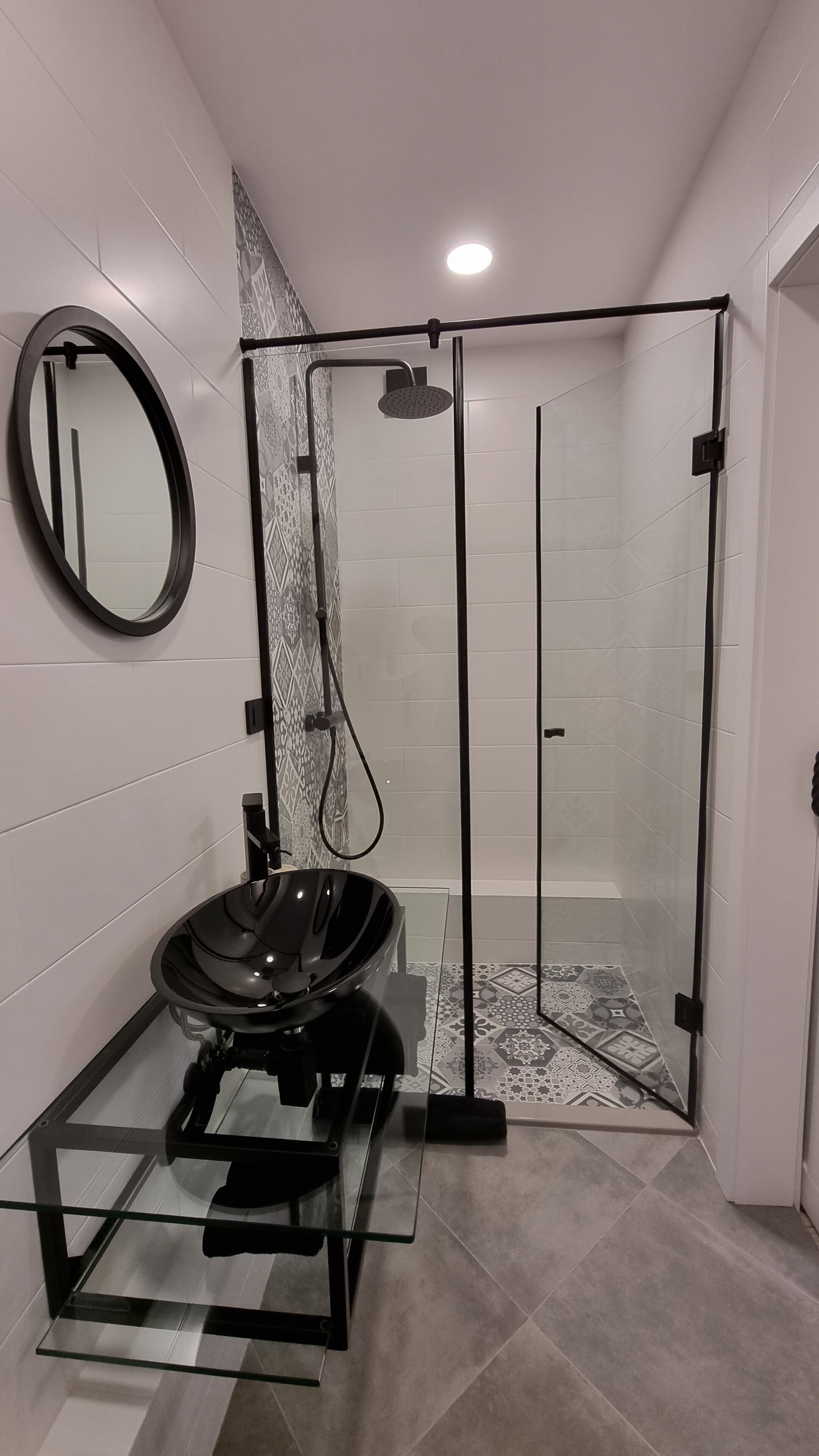 Une salle de bain moderne avec une douche à parois de verre, un miroir rond et un meuble-lavabo en verre avec un lavabo noir.