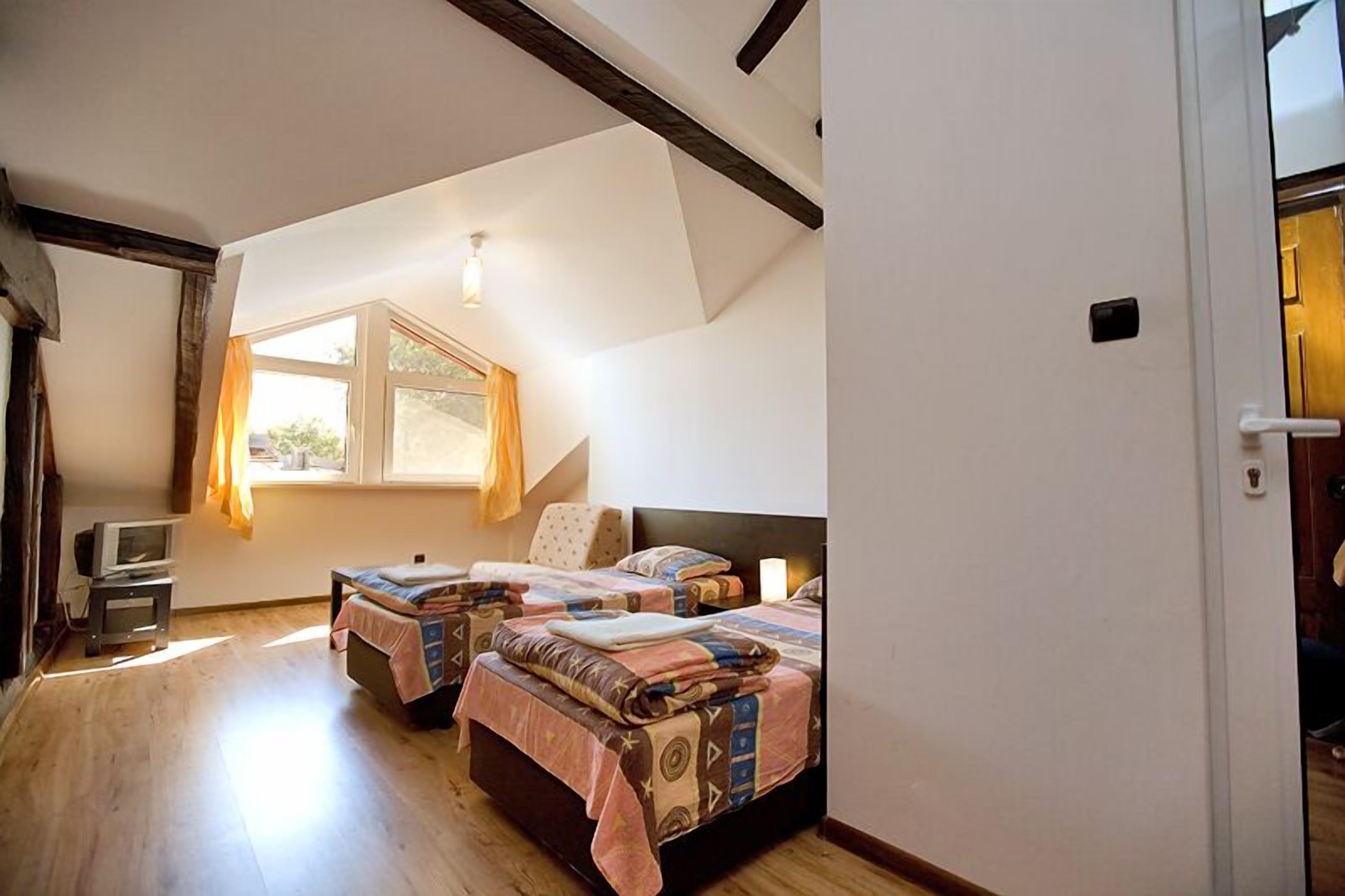Un dormitorio con dos camas, una ventana con cortinas, una mesita con un televisor y suelo de madera.
