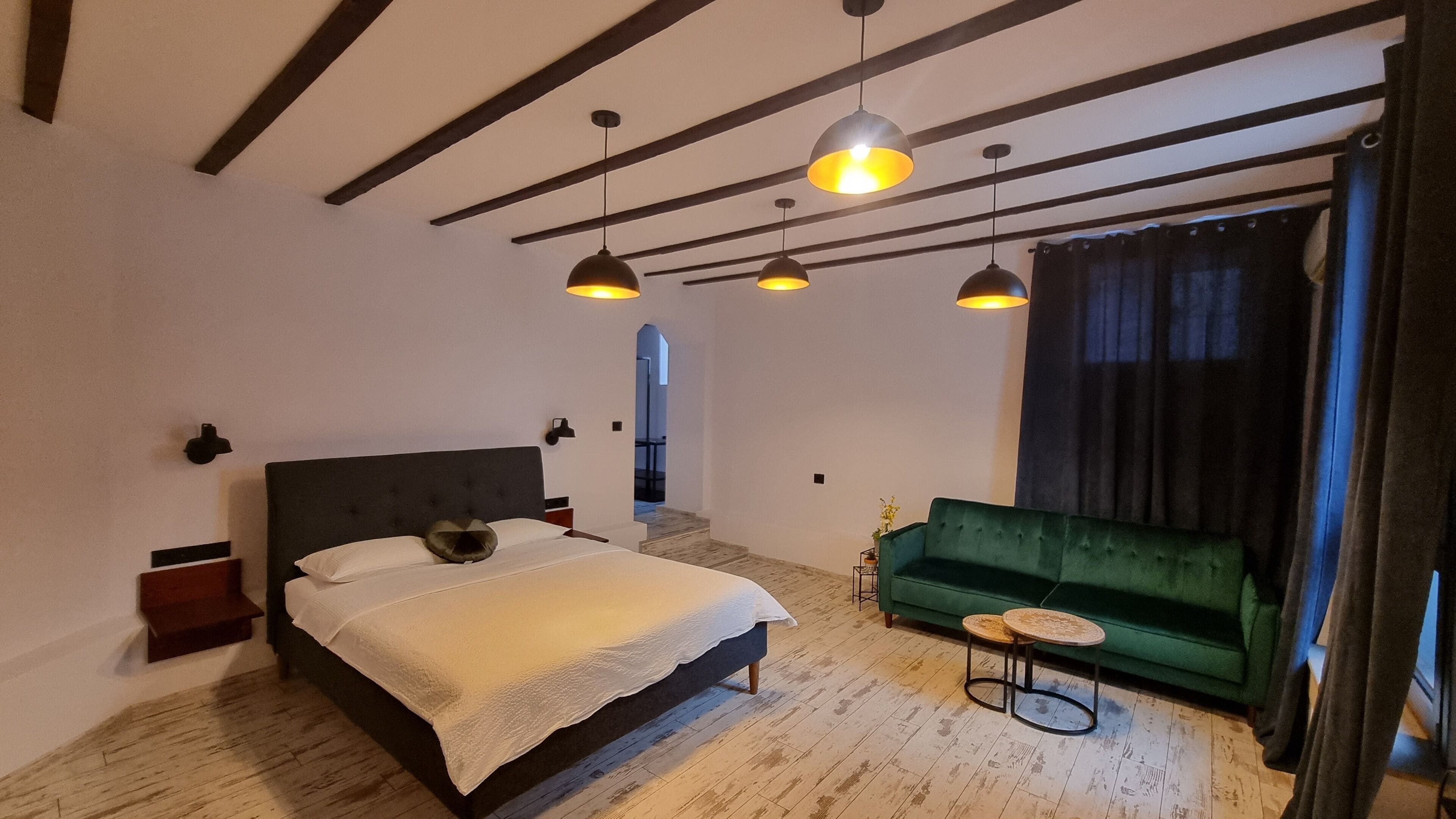A bedroom with a bed, a green sofa, and pendant lights.