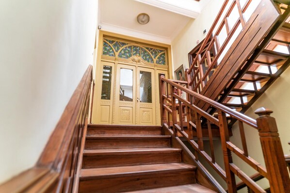 Una escalera de madera con barandilla que lleva a una puerta con paneles de vidrio emplomado.