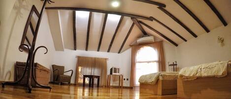 A room with wooden flooring, a bed, a chair, a table, and a ceiling with exposed beams.