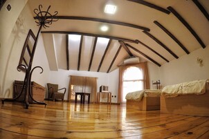 Quarto com piso de madeira, cama, cadeira, mesa e teto com vigas aparentes.