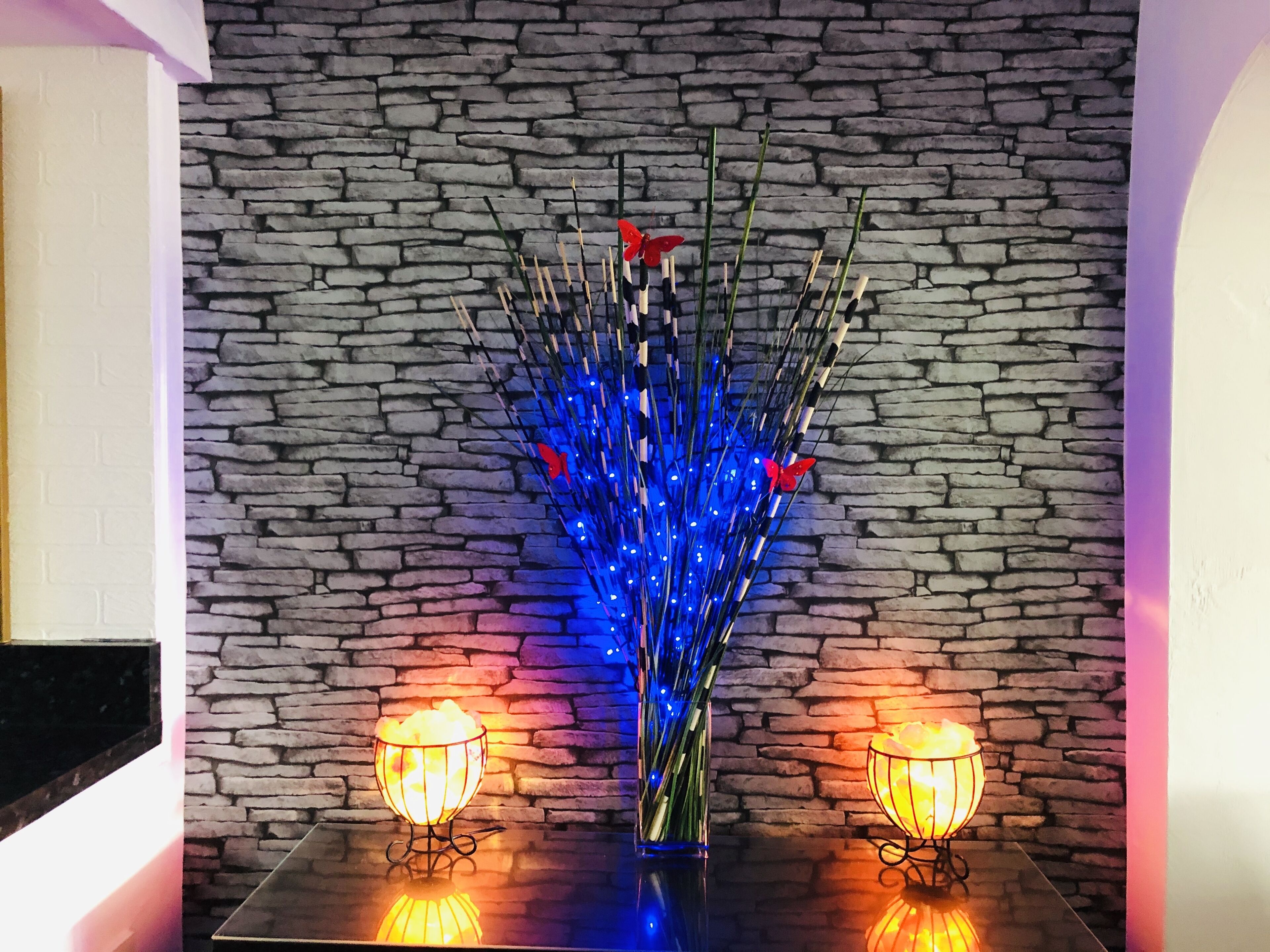 Una mesa con un centro de mesa decorativo que incluye luces azules y mariposas rojas, frente a una pared de piedra.