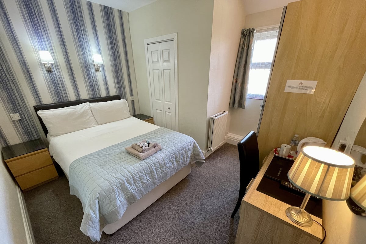 A neatly arranged hotel room with a bed, bedside table, lamp, and a small desk area.