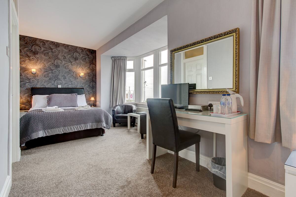 A hotel room with a bed, a desk, a chair, a mirror, and a window.