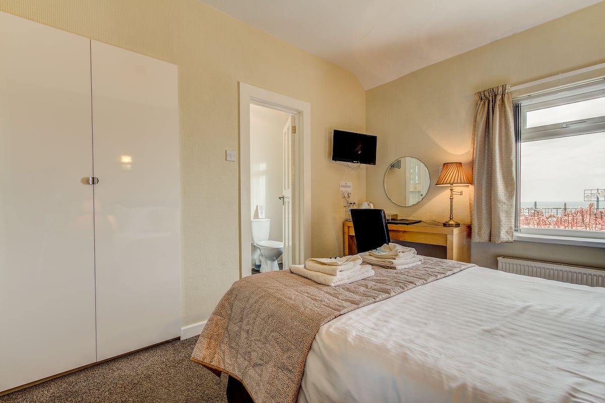 A hotel room with a bed, a desk with a chair, a television, a window with curtains, and a wardrobe.