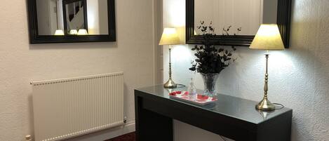 A hotel room with a black console table, two wall-mounted lamps, a mirror, a radiator, and a floral-patterned carpet.