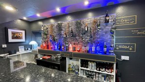 Zona de bar con temática oscura, que presenta una pared de piedra, varias botellas y un letrero que dice 'Welcome'.