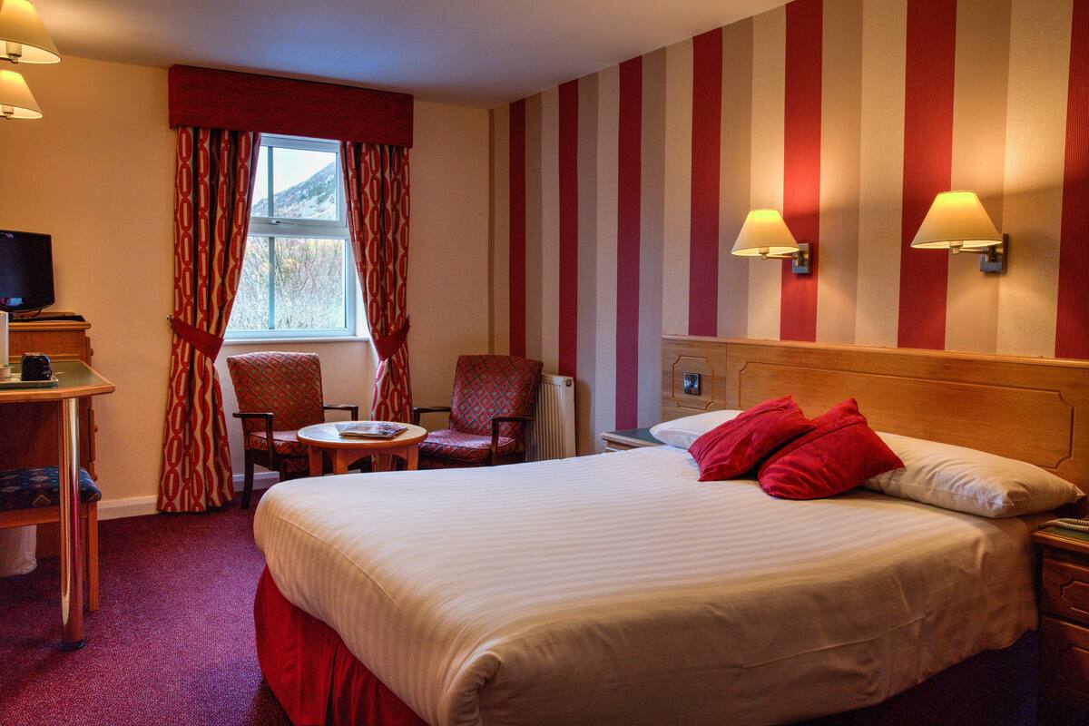A hotel room with a large bed, a desk with a television, a chair, and a window with curtains.