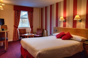 A hotel room with a large bed, a desk with a television, a chair, and a window with curtains. - Patterdale Hotel (Penrith)