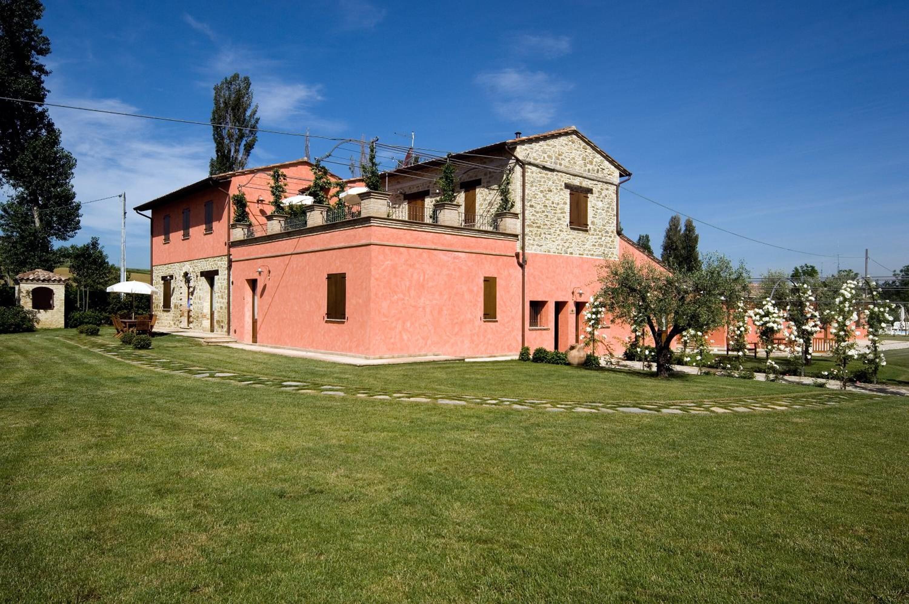 A two-story building with a pink facade, stone accents, and a small garden area with flowering plants.