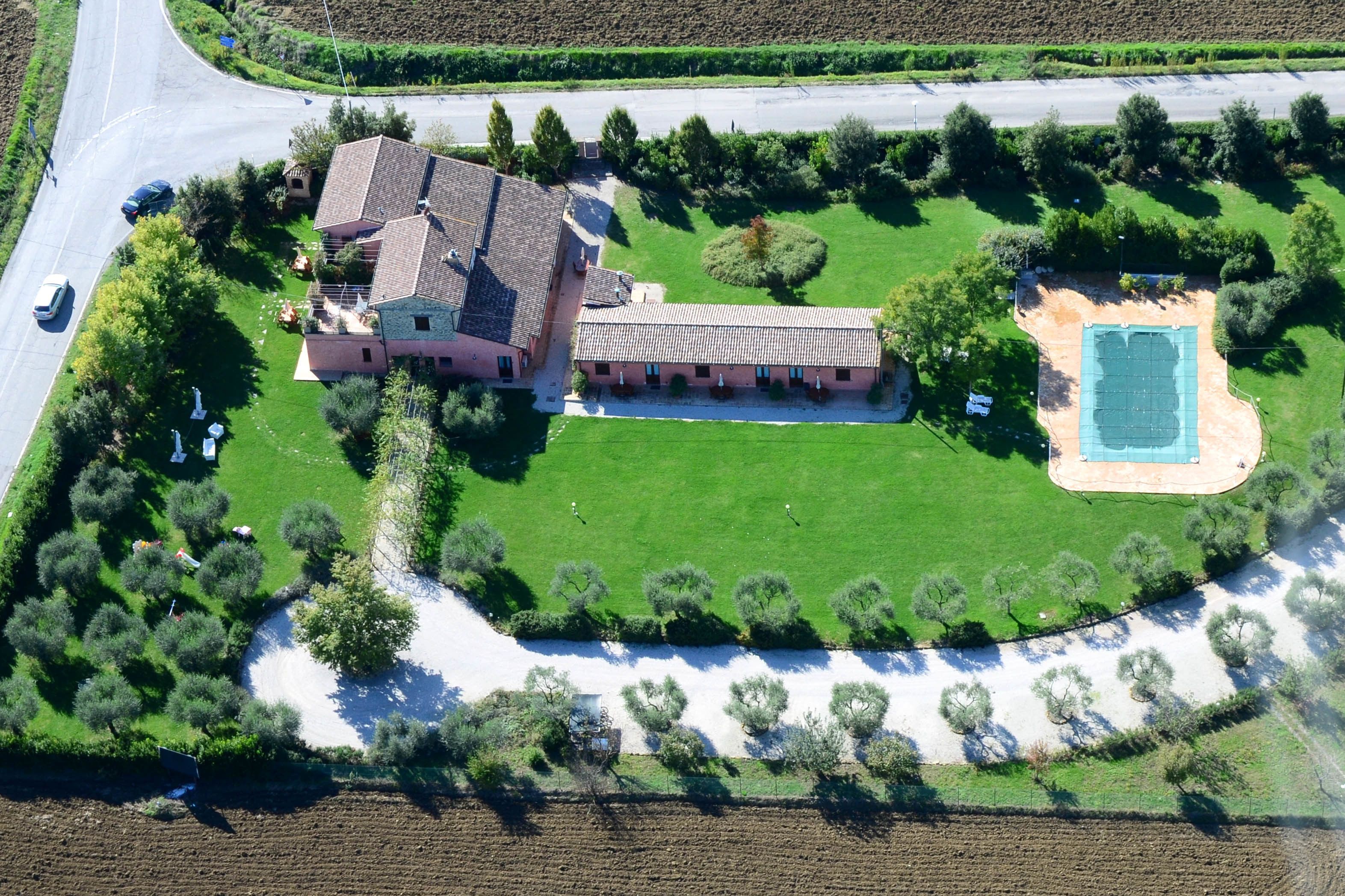 Vista aérea de una extensa propiedad con una casa principal, piscina y césped bien cuidado.