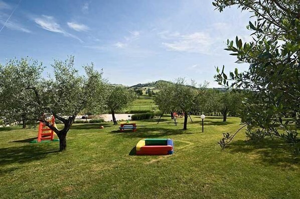 A grassy area with trees and colorful play equipment. - Casale Le Selvette (Perugia)