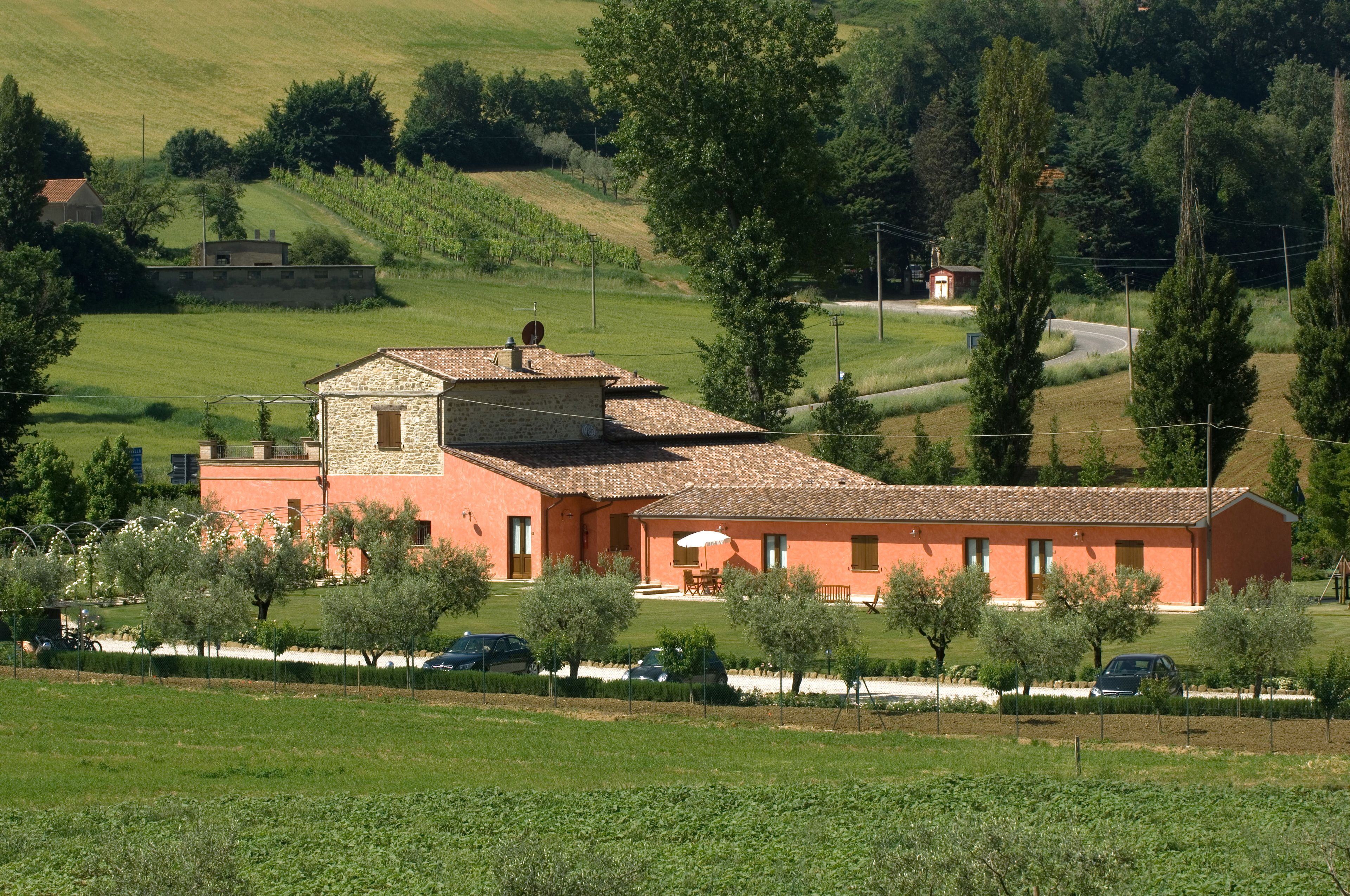Un edificio in pietra con tetto a tegole, immerso in una proprietà recintata con alberi e un cielo sereno.