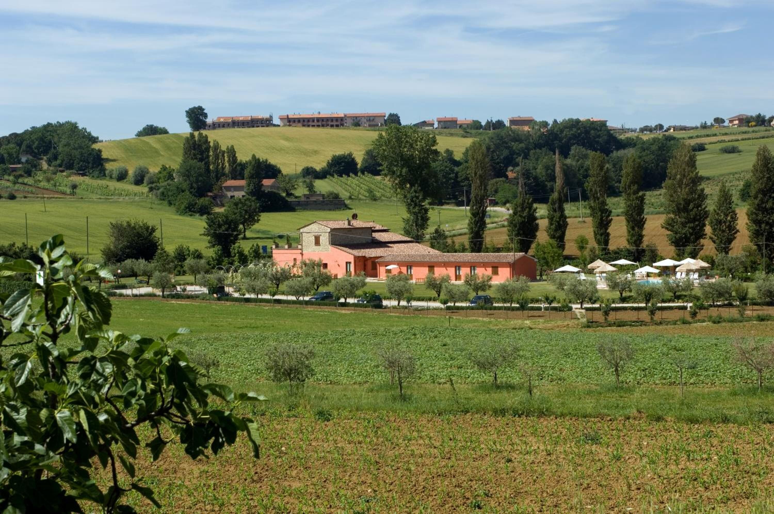 Ländliche Landschaft mit einem markanten roten Gebäude, umgeben von grünen Feldern und Bäumen.