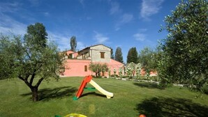 A grassy area with a playground, a tree, and a building in the background.
