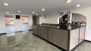 Un área de recepción con mostrador de madera, un reloj y un refrigerador.