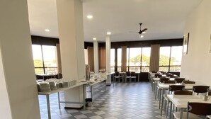 Un amplio comedor con suelo a cuadros, varias mesas y sillas, y grandes ventanales que aportan luz natural.