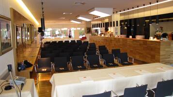 Un salón de conferencias con filas de sillas, una mesa larga y una zona de recepción con mostrador y barra.