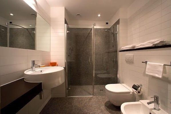 Un baño moderno con ducha envuelta en vidrio, lavamanos blanco y un inodoro.